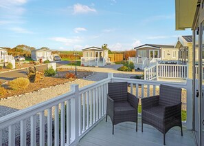 Eine Terrasse mit zwei Korbstühlen, einem weißen Geländer und Blick auf Mobilheime im Hintergrund.