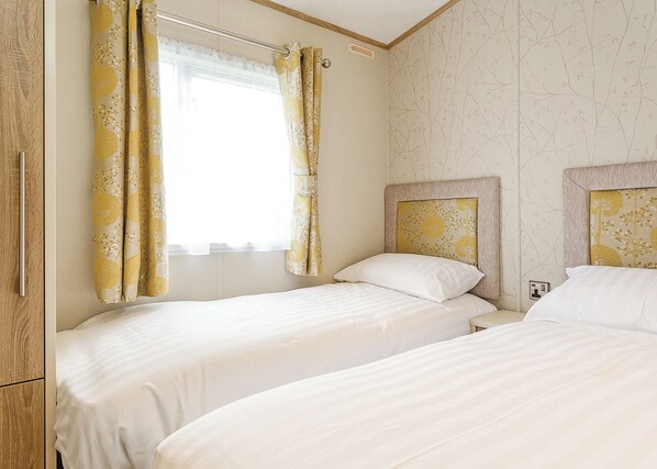 Ein Hotelzimmer mit zwei Betten, einem Fenster mit Vorhängen und einer Wand mit floralem Muster.