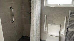 A bathroom with a shower, toilet, and handrails. - 1 bedroom accommodation in Hawes, (Hawes,)