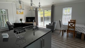 A modern kitchen with a central island, pendant lights, a dining area with a table and chairs, and a TV in the background. - 1 bedroom accommodation in Hawes, (Hawes,)