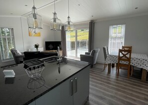 A modern kitchen with a central island, pendant lights, a dining area with a table and chairs, and a TV in the background. - 1 bedroom accommodation in Hawes, (Hawes,)