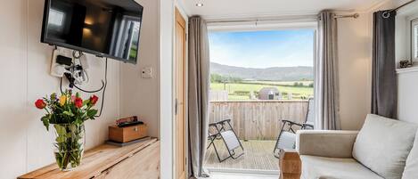 Une chambre dotée d’une télévision, d’un bureau en bois, d’un canapé et d’un balcon offrant une vue sur la campagne.