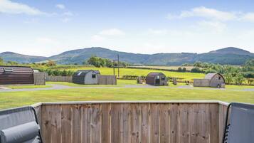 Une terrasse avec deux chaises, une clôture en bois et plusieurs petits abris de jardin, le tout situé dans un cadre rural avec des collines en arrière-plan.