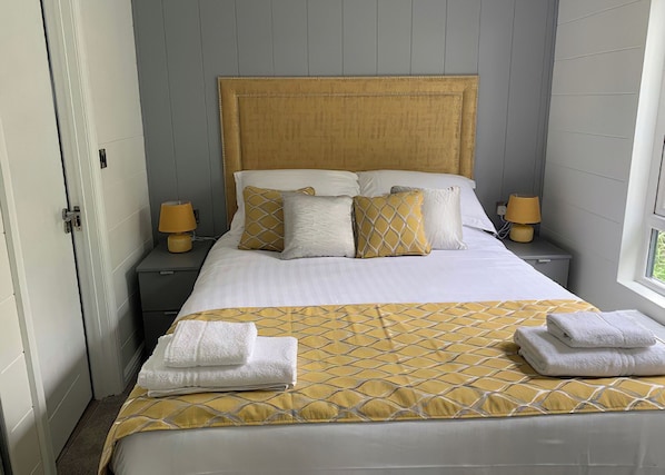A neatly made bed with a patterned bedspread, two bedside lamps, and two folded towels on the bed.
