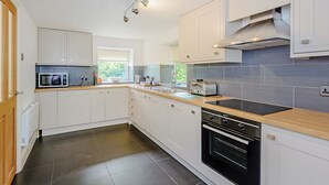 Una cocina moderna con armarios blancos, un horno negro, una campana extractora de acero inoxidable y un ventanal que proporciona luz natural.