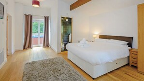 Un dormitorio con una cama grande, suelo de madera, una alfombra pequeña, cabecera de madera y una zona de ducha.