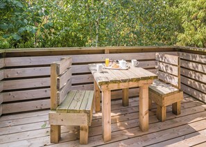 A wooden deck with a table and benches, surrounded by greenery.
