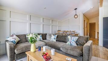 A modern living room with a grey sectional sofa, a wooden coffee table with fruit, and a vase of flowers.