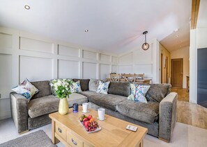 A modern living room with a grey sectional sofa, a wooden coffee table with fruit, and a vase of flowers.