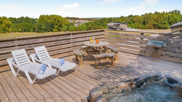 Terraza de madera con sillones de descanso, una mesa y un jacuzzi.