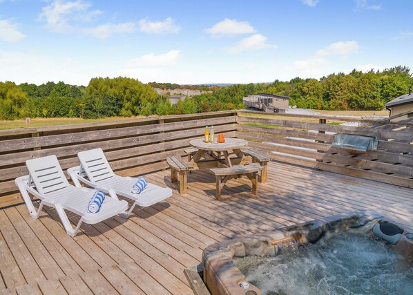 A wooden deck with lounge chairs, a table, and a hot tub.