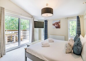 A bedroom with a bed, a TV, a window with curtains, and a view of greenery outside.