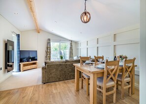 A modern living room with a flat-screen TV, sofa, dining table with chairs, and a hanging light fixture.