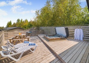 A wooden deck with a hot tub, lounge chairs, and a table.