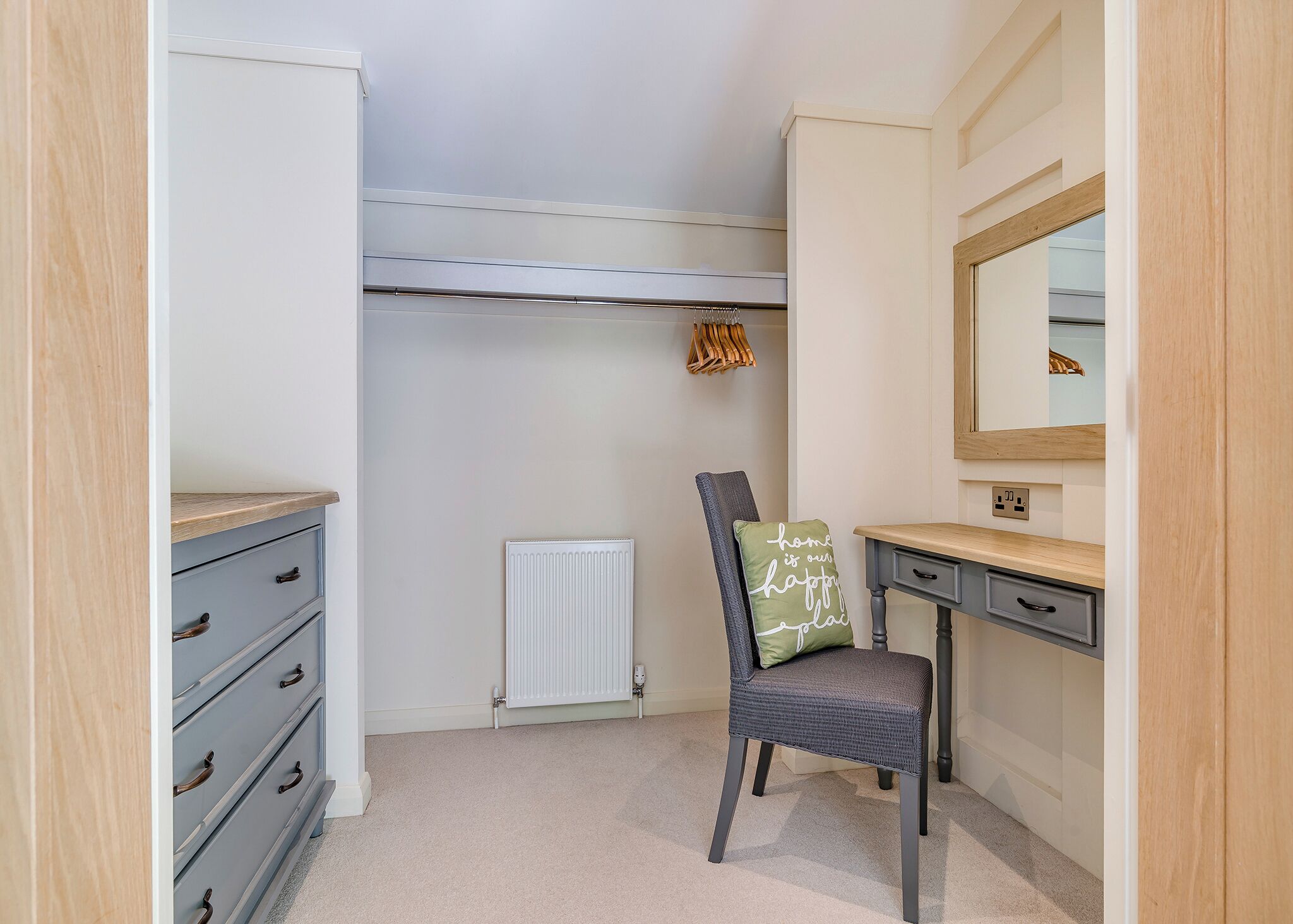 A bedroom with a bed, a dresser, a chair with a pillow, a desk, a radiator, and a mirror.