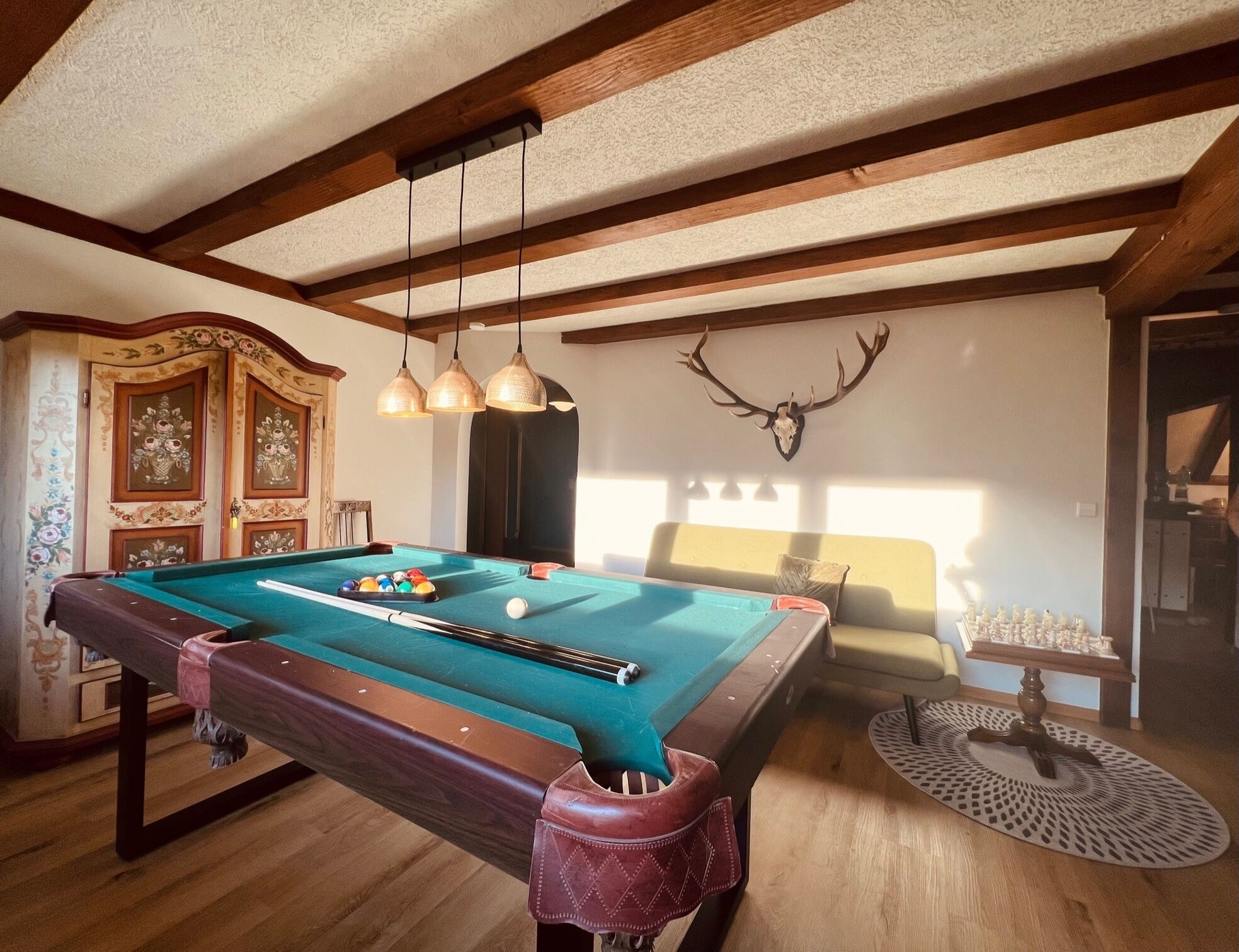 A pool table with balls, a wooden ceiling, and a deer skull wall decoration.