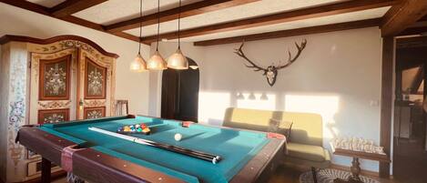 A pool table with balls, a wooden ceiling, and a deer skull wall decoration.