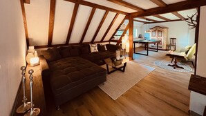 Une pièce chaleureuse de style loft, avec des poutres apparentes, un canapé d’angle foncé, une table de billard et un plancher en bois rustique.