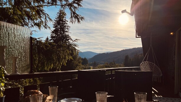 Une table dressée à l’extérieur, avec de la nourriture et des boissons, offrant une vue sur un paysage montagneux.