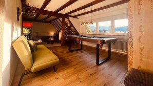 Une pièce chaleureuse avec une table de billard, un fauteuil confortable et une vue sur l’extérieur grâce à de grandes fenêtres.