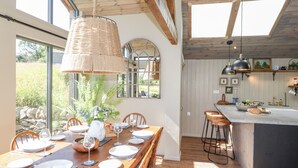 A dining area with a wooden table set for six, a large woven light fixture, and a view of the kitchen with a bar area. - The Owl's Shack (Kendal)