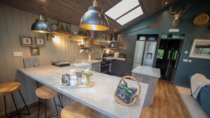 A modern kitchen with a central island, bar stools, pendant lighting, and a view of the outdoors. - The Owl's Shack (Kendal)