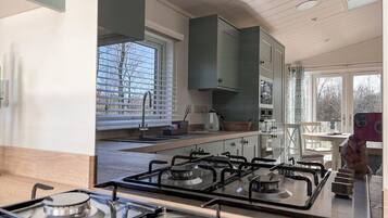 Une cuisine moderne équipée d’une cuisinière à gaz, d’un évier et d’une fenêtre avec des stores.
