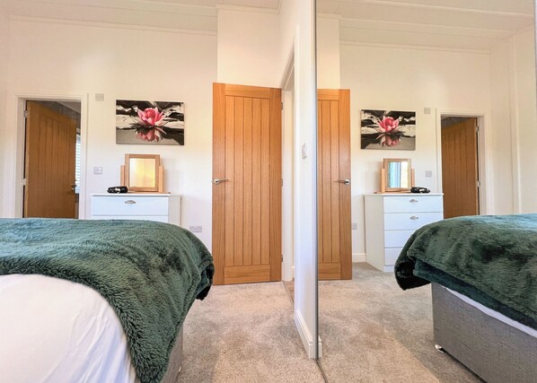Un dormitorio con dos camas, una puerta de madera, un aparador y un espejo.