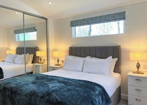 A hotel room with a large bed, bedside tables, a mirror, and a window with a view of trees.