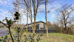 Une maison dotée d’une terrasse, entourée d’arbres et d’herbe.