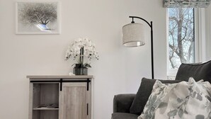 Un salon avec un canapé gris, un meuble en bois doté d’une porte coulissante, un lampadaire et un tableau encadré accroché au mur.
