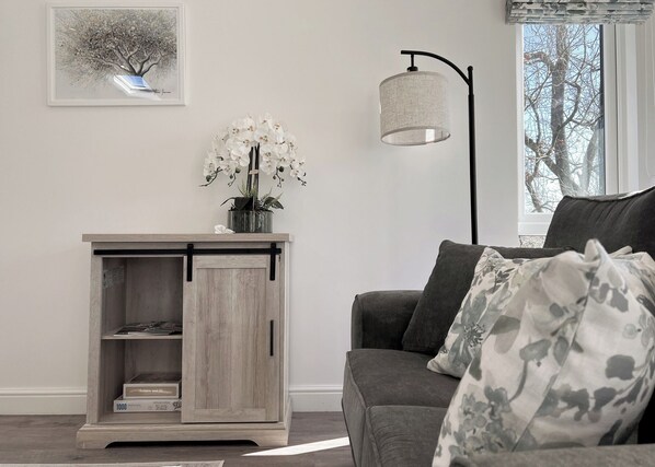 A living room with a grey sofa, a wooden cabinet with a sliding door, a floor lamp, and a framed picture on the wall.