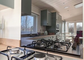 Una cocina moderna con estufa a gas, pileta y ventana con persianas.