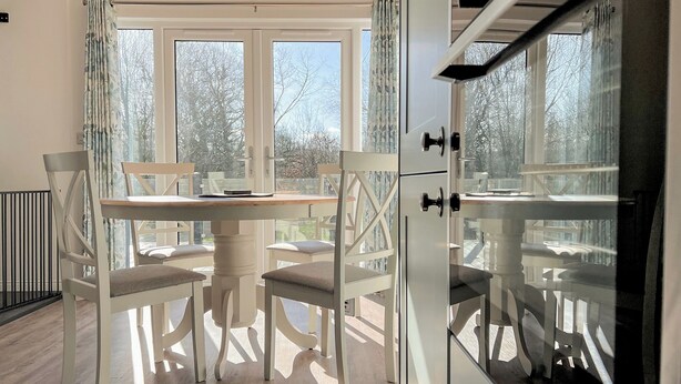 Une pièce comprenant une table à manger, des chaises et offrant une vue sur l’extérieur grâce à de grandes fenêtres.