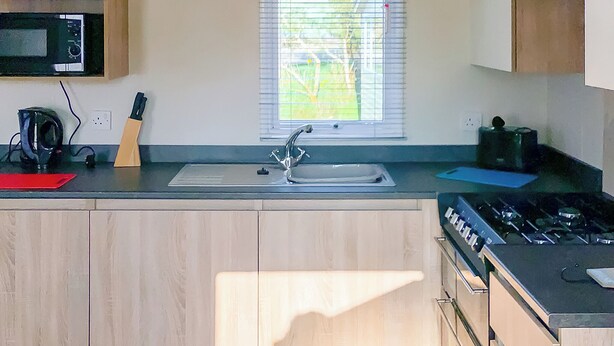 A kitchen with a microwave, sink, stove, and cabinets. - New for 2019. Contemporary caravan with one double and two twin. (Cargill)