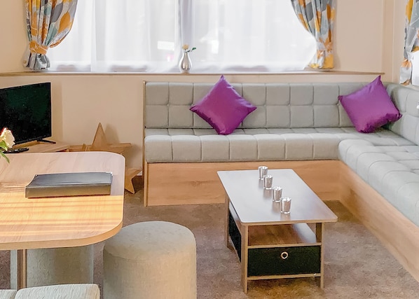 Ein modernes Zimmer mit Sofa, Couchtisch, Fernseher und einem Fenster mit Vorhängen.