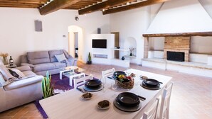 A spacious living area with a high ceiling, a fireplace, a sofa, a dining table set for four, and a television mounted on the wall. - Castellaccia contemporary country house  (San Gimignano)