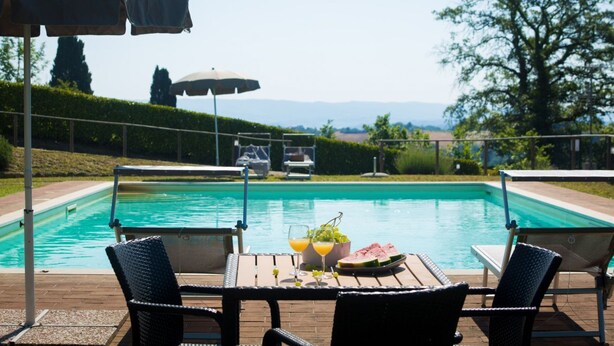 A poolside area with a table set for two, a pool, and umbrellas. - Castellaccia contemporary country house  (San Gimignano)