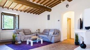 A living room with a beige sofa, a glass coffee table, and a purple rug. There is a window with a view of greenery outside. - Castellaccia contemporary country house  (San Gimignano)
