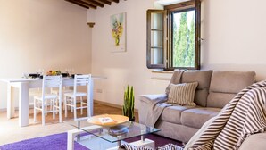 A living room with a dining area, a sofa, a glass coffee table, and a window with a view of trees. - Castellaccia contemporary country house  (San Gimignano)