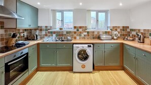 A compact kitchen with a washing machine, wooden flooring, and a view through the windows. - Cornish end terraced cottage with one double and one twin. (Tintagel)