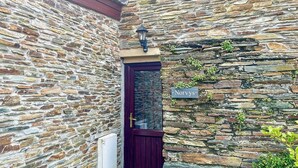 A stone building with a dark wooden door and a window. A sign on the wall reads "Norvys." - Cornish end terraced cottage with one double and one twin. (Tintagel)