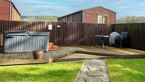 A backyard with a wooden deck, a hot tub, a table, chairs, and a barbecue grill. - Cornish end terraced cottage with one double and one twin. (Tintagel)