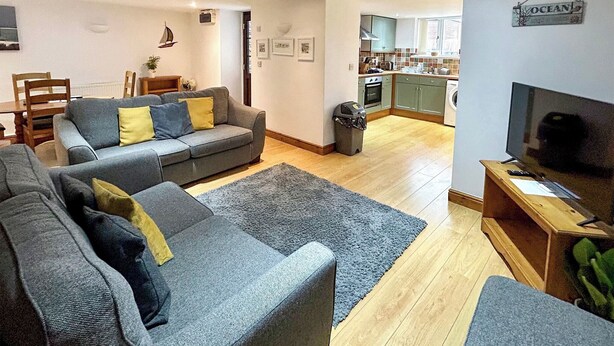 A modern living room with grey sofas, a wooden coffee table, and a TV stand. - Cornish end terraced cottage with one double and one twin. (Tintagel)