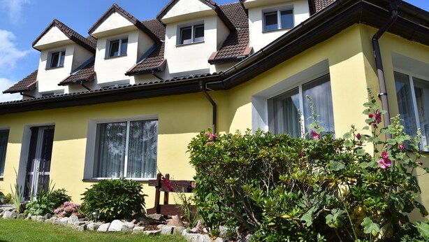 A two-story house with a yellow facade, multiple windows, and a well-maintained garden with various plants and flowers. - Willa Białe Piaski (Krokowa)