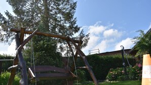 A wooden swing set in a garden with a bench and a tree in the background. - Willa Białe Piaski (Krokowa)