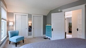 Ein Schlafzimmer mit einem großen Bett, einem blauen Sessel, einer Kommode und einem Kleiderschrank mit zwei Türen.