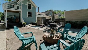 Ein Garten mit überdachter Terrasse, Sitzgelegenheiten und einem Feuerkorb.