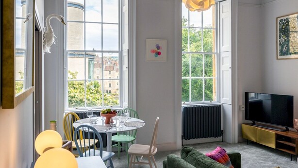 A modern living room with a dining area, large windows, a television, and a green sofa. - Stunning one bed apartment in central location - Pass the Keys (Bath)