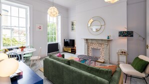 A living room with a green sofa, a TV, a fireplace, and a dining area with a table and chairs. - Stunning one bed apartment in central location - Pass the Keys (Bath)